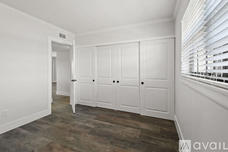 A room with white walls and wooden flooring with a set of four doors.