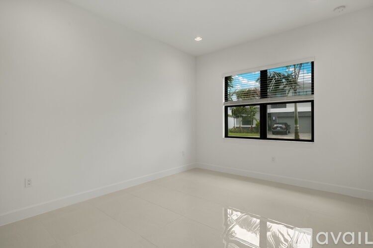 A large empty room with a window and a view of trees and a house outside.