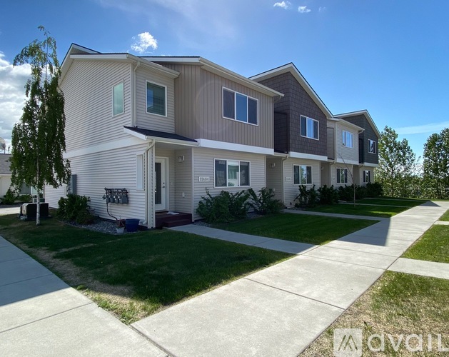 A row of houses with the first one on the left being a two story building with a tan and white exterior and the rest being one story buildings with a white and grey exterior.