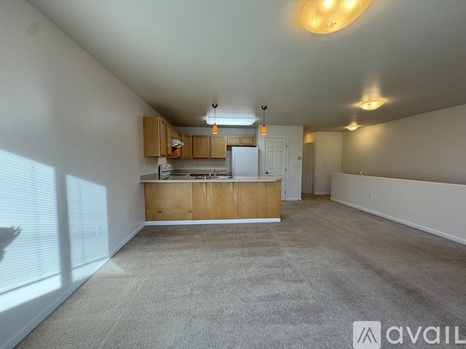 A spacious, empty room with a kitchenette and carpeted floor.