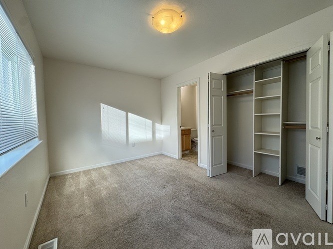 A room with a carpeted floor and a large window with blinds.