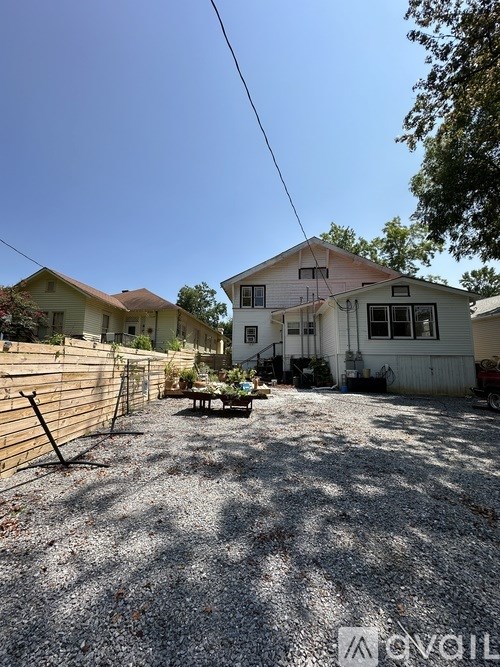 A gravel driveway leads to a white house with a brown fence.