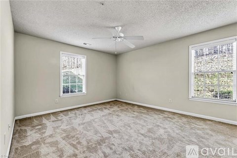 A room with a carpeted floor, a ceiling fan, and two windows.