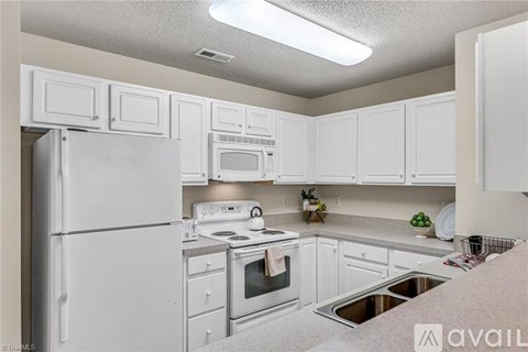 A white kitchen with a refrigerator, microwave, oven, and sink.