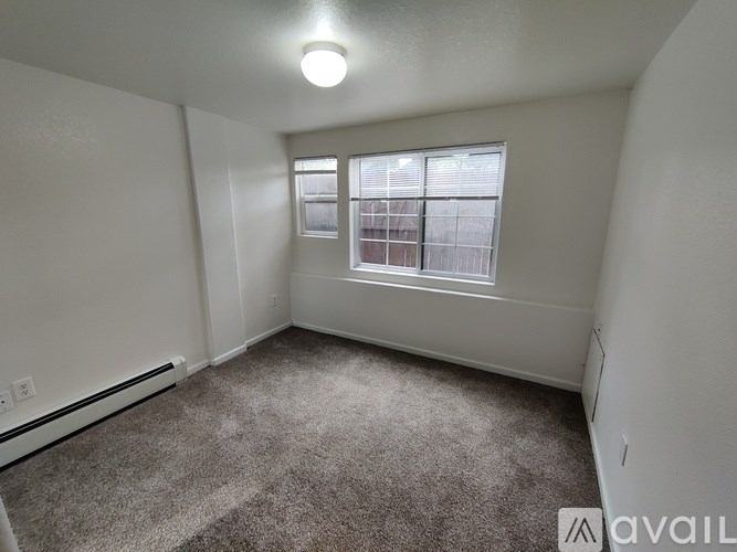 A room with a carpeted floor, a window with blinds, and a wall-mounted air conditioner unit.