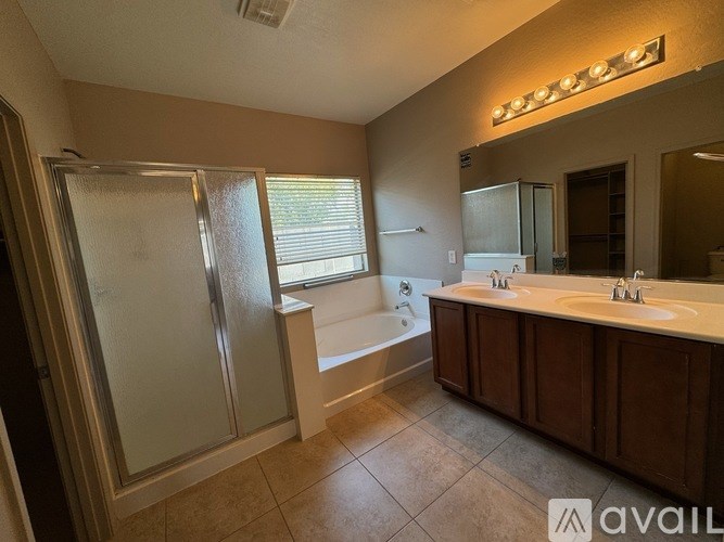 A bathroom with a glass shower door, a bathtub, and a double sink vanity.