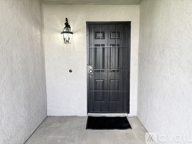 A black door with a metal grill is set in a white wall.