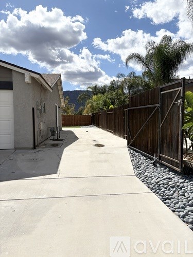 A concrete pathway leads to a house with a wooden fence on one side and a garage door on the other.