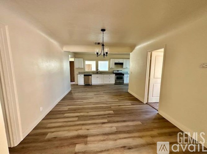 A spacious room with wooden flooring and a chandelier hanging from the ceiling.