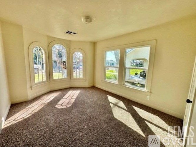 A sunny room with carpet flooring and three windows.