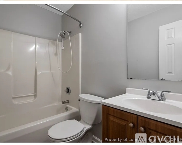 A white toilet is in a bathroom with a white tub and sink.