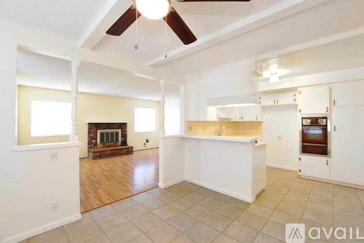 A spacious living room with a fireplace and a kitchen area in the background.