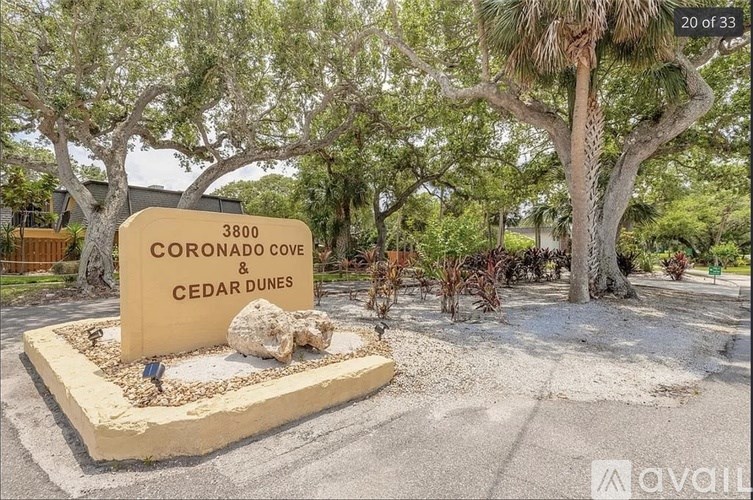 A sign for Coronado Cove Cedar Dunes is displayed in front of a tree.