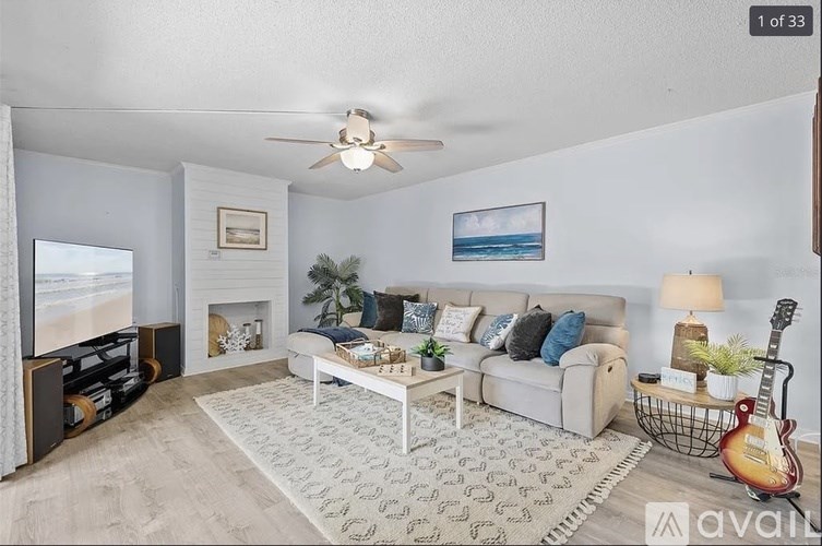A living room with a white couch, a fireplace, and a guitar on the side table.