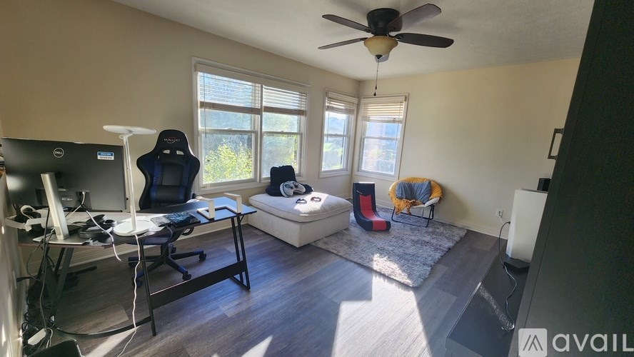A room with a ceiling fan, a desk with a computer, and a window with blinds.