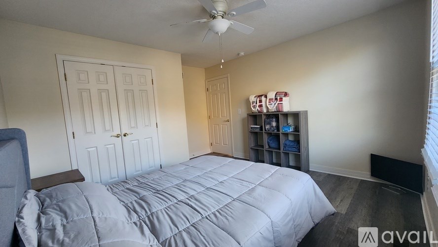A bedroom with a bed, a ceiling fan, and a shelf with boxes on it.