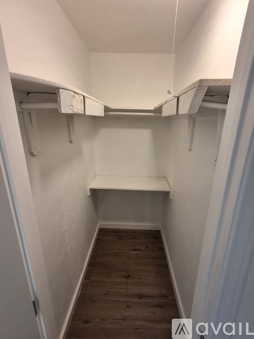 A small, white closet with a bench and a wooden floor.