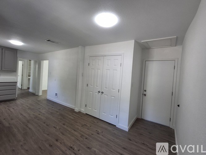 A room with white walls and wooden flooring, with a door on the right side.
