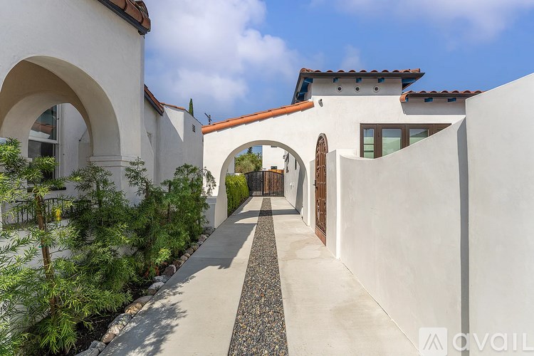 A white building with a red tile roof and a stone pathway leading to an arched doorway.