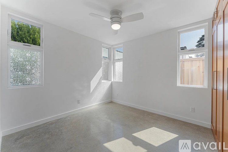 A spacious room with a ceiling fan and a window overlooking a tree-filled area.