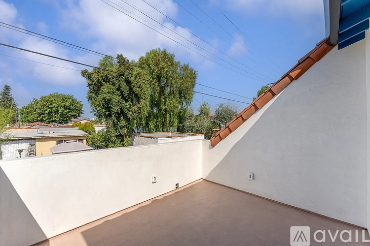 A balcony with a white wall and a brown roof overlooks a residential area.