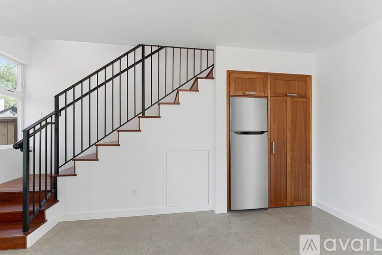 A black metal staircase with wooden steps and railings leads to a white wall with a wooden door and a metal trash can.