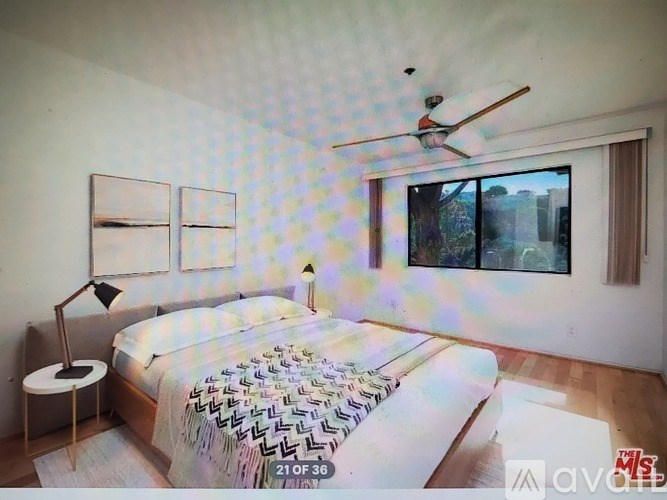 A bedroom with a bed, a ceiling fan, and a window with a view of the city.