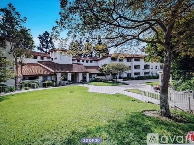 A large white building with a red roof is surrounded by a green lawn and trees.