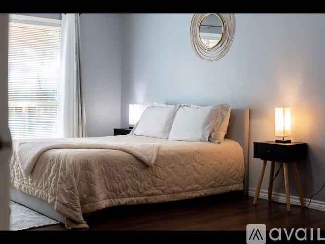 A bedroom with a bed, a side table with a lamp, and a round mirror on the wall.