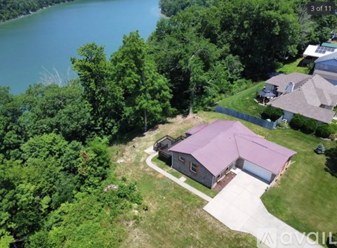 A house with a purple roof is surrounded by trees and a body of water.