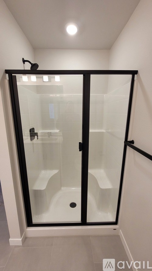 A glass shower stall with a black frame and a drain in the middle.