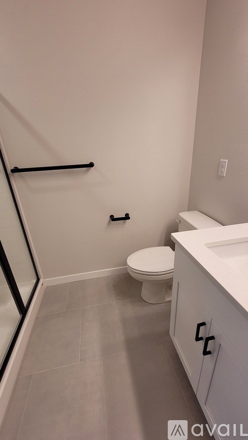 A bathroom with a toilet, sink, and a shower with a black frame.