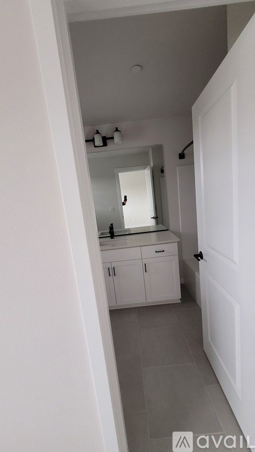 A white door is open to a bathroom with a mirror and cabinets.