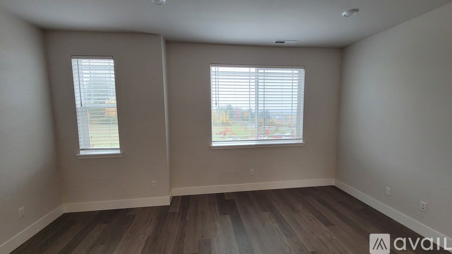 A room with two windows and wooden flooring is available for rent.