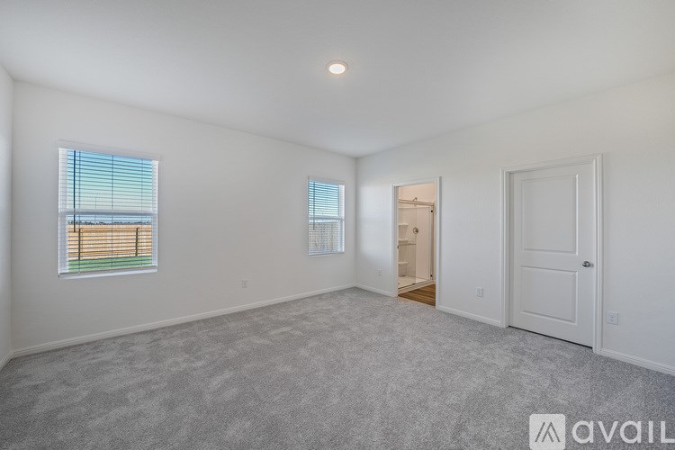 A spacious empty room with a carpeted floor and a window with blinds.