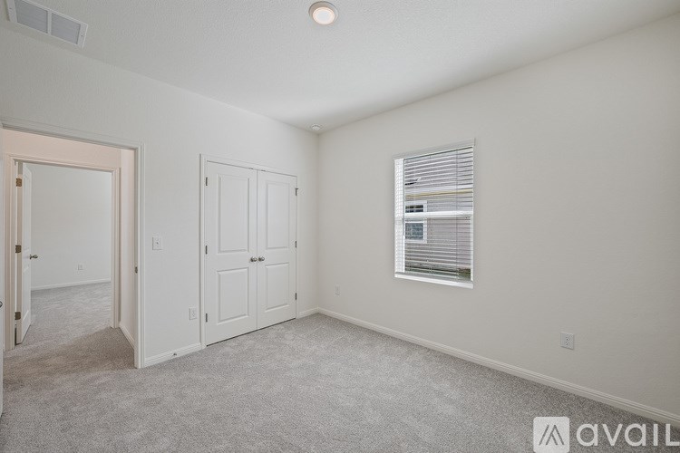 A spacious room with a carpeted floor, a window with blinds, and a door leading to another room.
