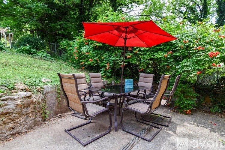 A patio with a table, chairs and a red umbrella.