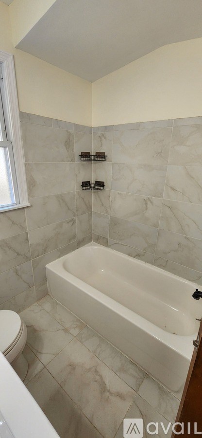 A bathroom with a white bathtub and tiled walls.