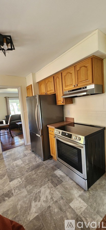 A kitchen with a black refrigerator and an oven with a yellow towel hanging on it.