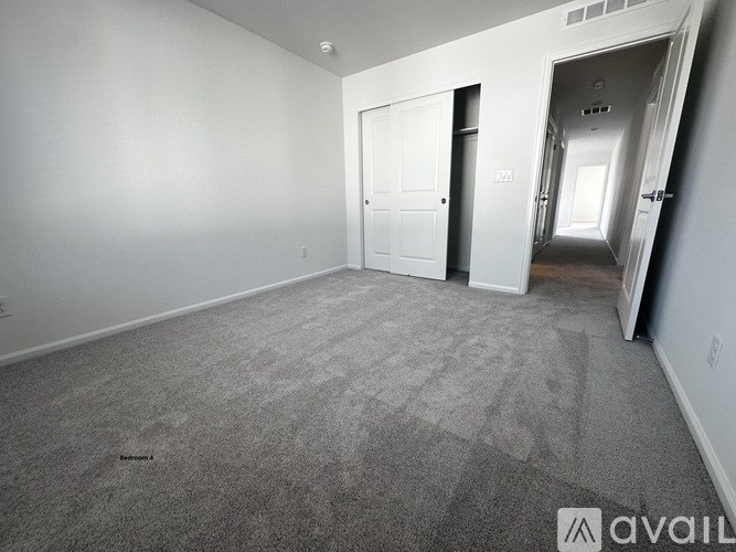 A spacious room with grey carpeting and white walls, featuring a door and a hallway.