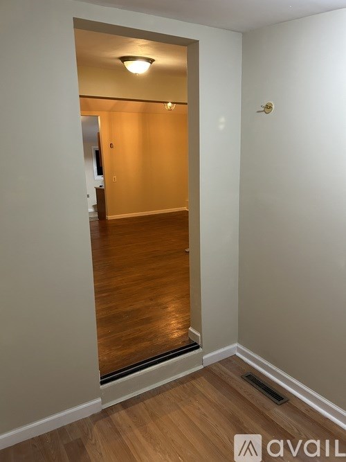A hallway with a wooden floor and white walls leading to a door.