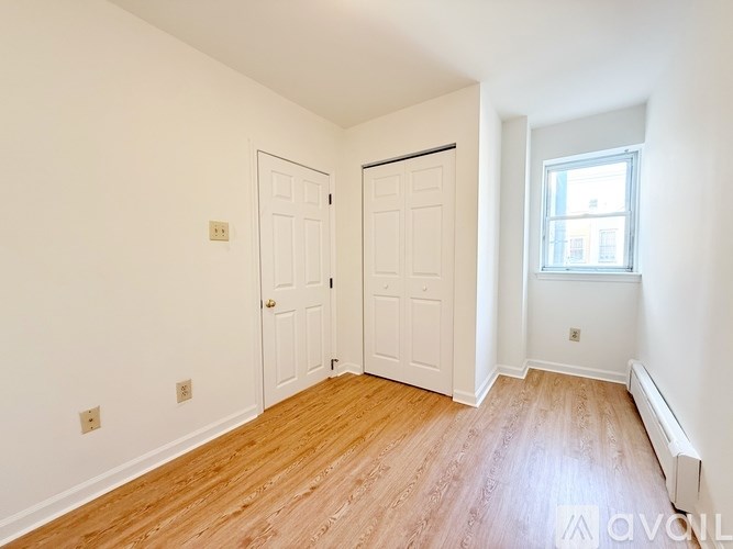 A room with wooden floors and white walls, featuring a door, a window, and a radiator.