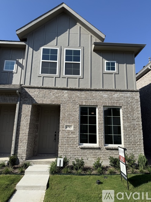 A house with a grey facade and a white sign in front.