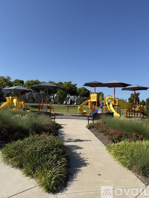A playground with a yellow slide and blue umbrellas.