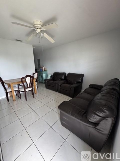 A living room with a black leather couch and a ceiling fan.