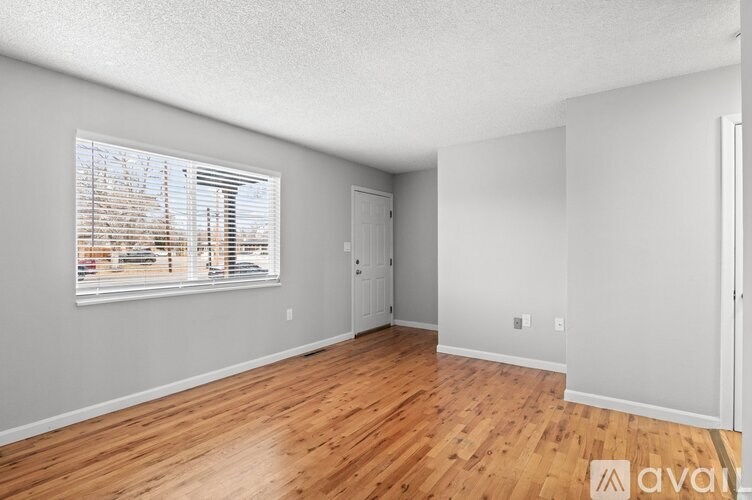 A room with wooden floors and a window showing a view of trees and buildings outside.