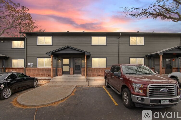 A red truck is parked in front of a building with a car parked to its left.