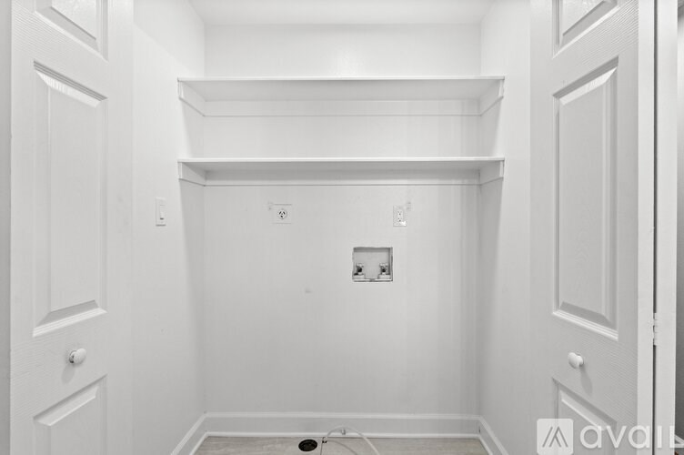 A white room with a door on the left and a shelf on the wall.