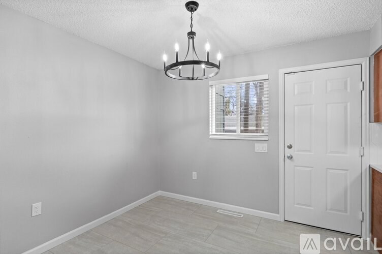 A chandelier hangs in a well-lit, empty room with a door and window.