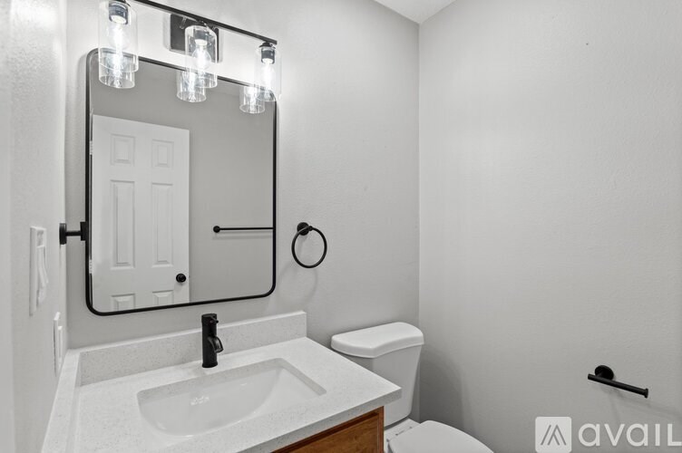 A bathroom with a sink, toilet, mirror, and lighting fixtures.